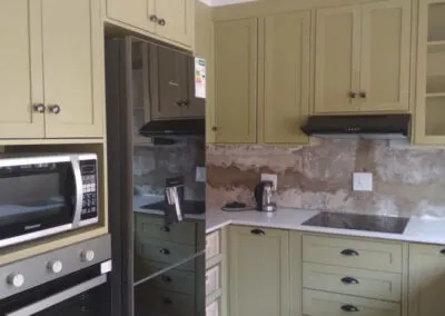 Sage green kitchen cabinetry beside a built-in fridge